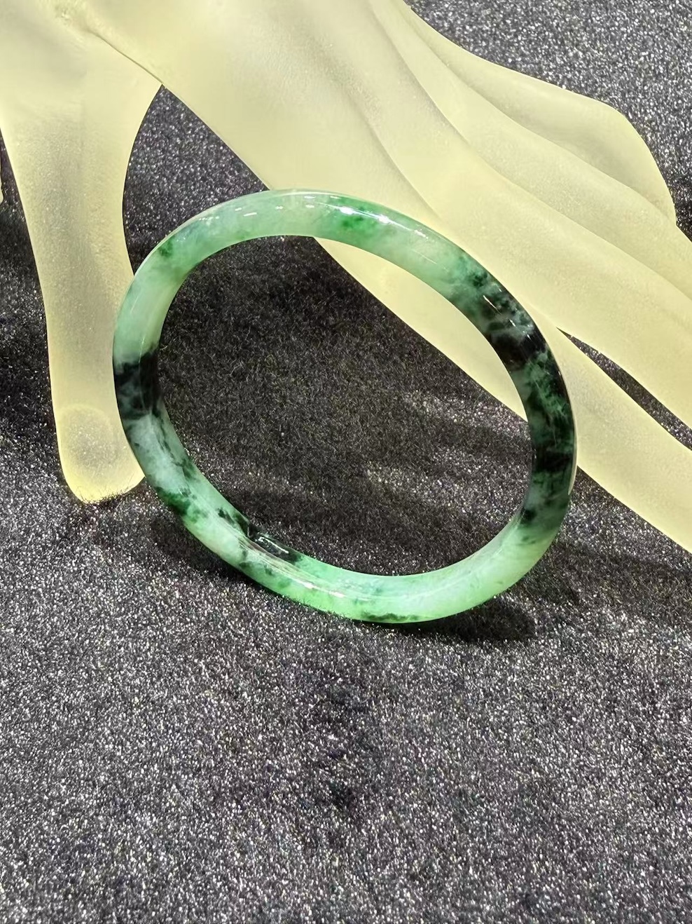 Old pit jadeite bangle in an oval shape, with translucent green jadeite carrying deeper green patches and natural dark inclusions