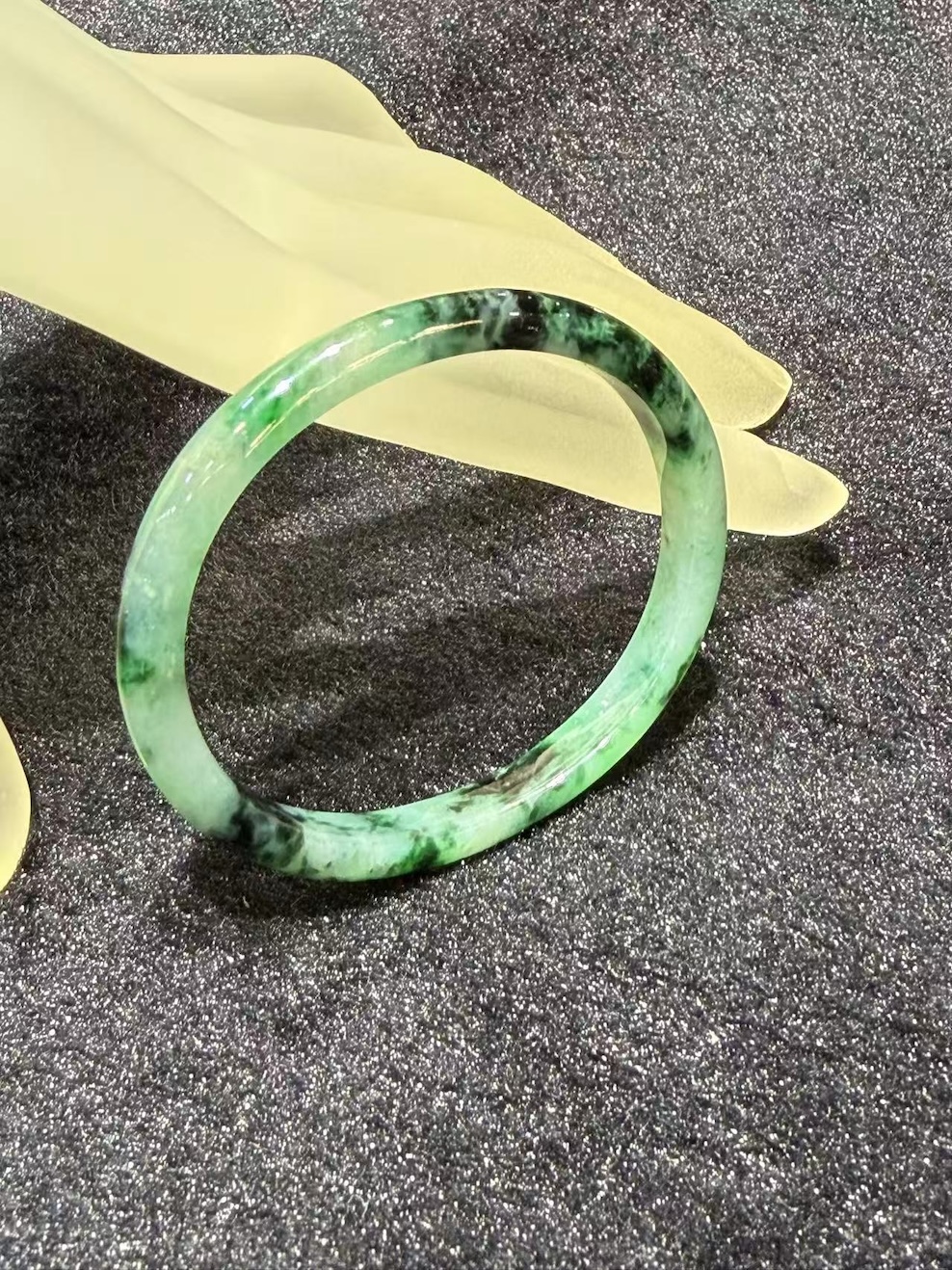 Old pit jadeite bangle in an oval shape, with translucent green jadeite carrying deeper green patches and natural dark inclusions