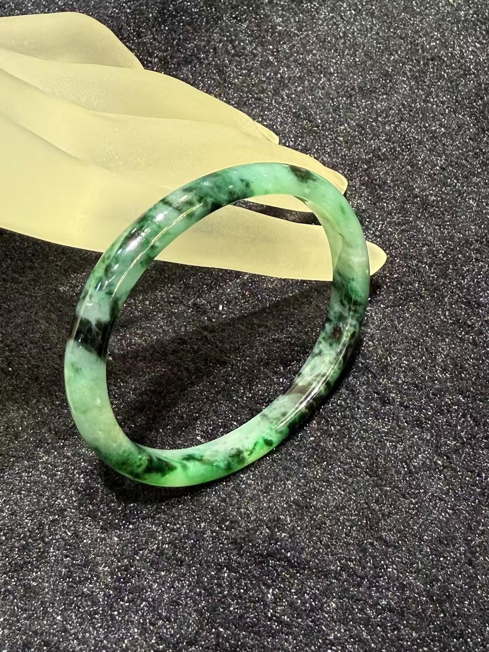 Old pit jadeite bangle in an oval shape, with translucent green jadeite carrying deeper green patches and natural dark inclusions