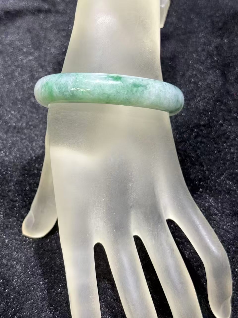 Light apple green jadeite bangle in an oval shape, with a translucent white base and soft apple green and faint bluish-green tones drifting across the ring