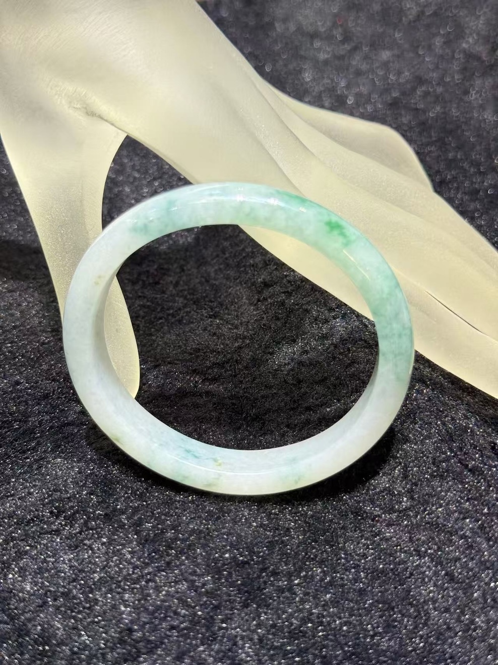 Light apple green jadeite bangle in an oval shape, with a translucent white base and soft apple green and faint bluish-green tones drifting across the ring