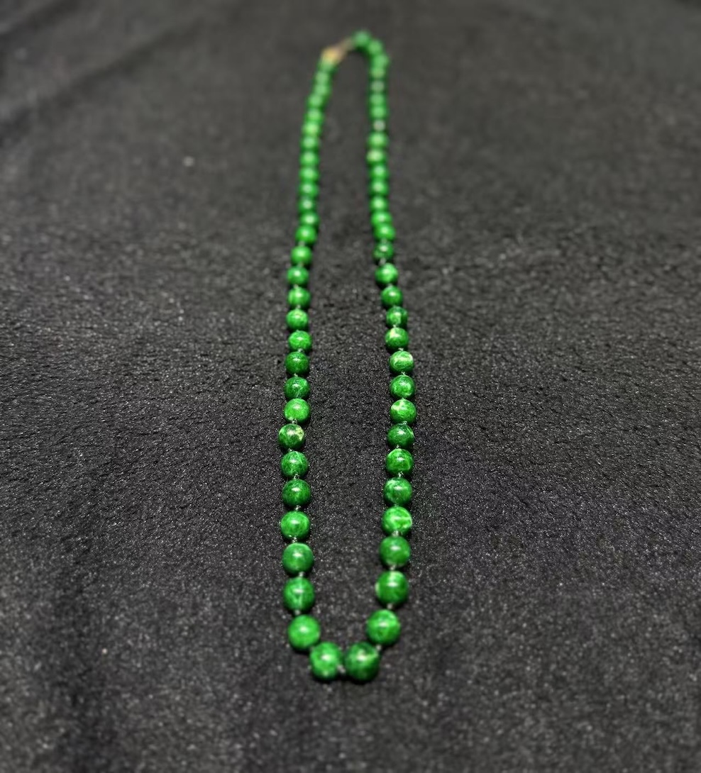 Green jade necklace strung with round vibrant green jadeite beads in an even, saturated tone, shown on a black necklace display bust