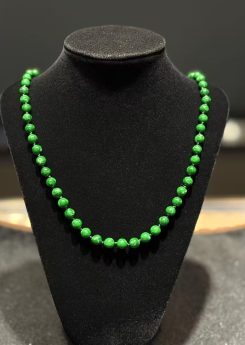 Green jade necklace strung with round vibrant green jadeite beads in an even, saturated tone, shown on a black necklace display bust