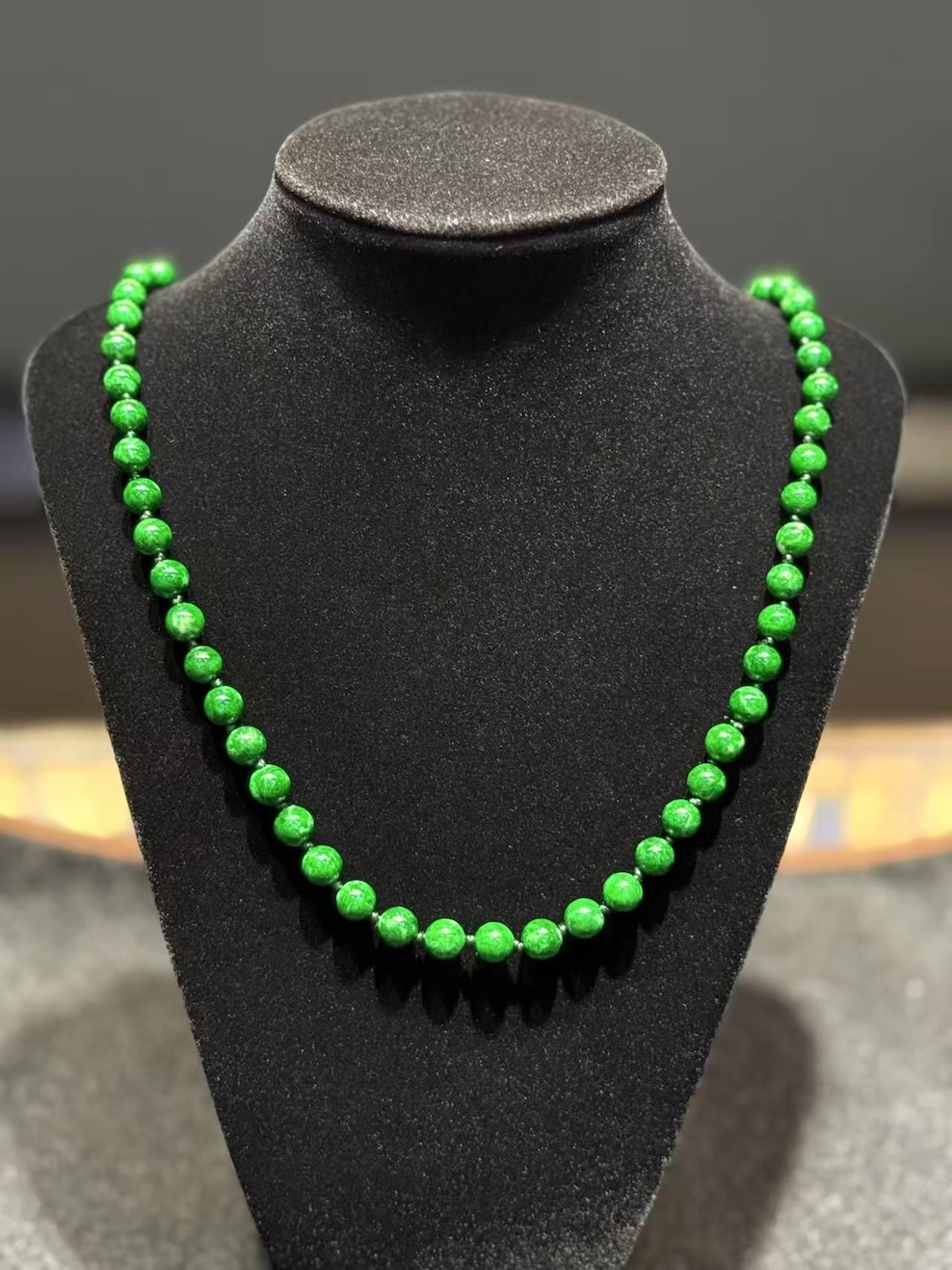 Green jade necklace strung with round vibrant green jadeite beads in an even, saturated tone, shown on a black necklace display bust