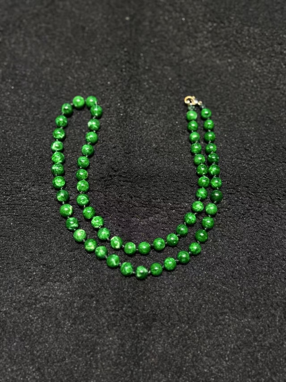 Green jade necklace strung with round vibrant green jadeite beads in an even, saturated tone, shown on a black necklace display bust