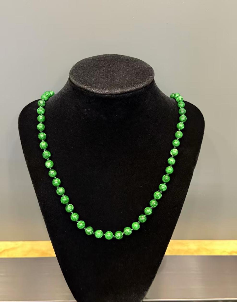 Green jade necklace strung with round vibrant green jadeite beads in an even, saturated tone, shown on a black necklace display bust