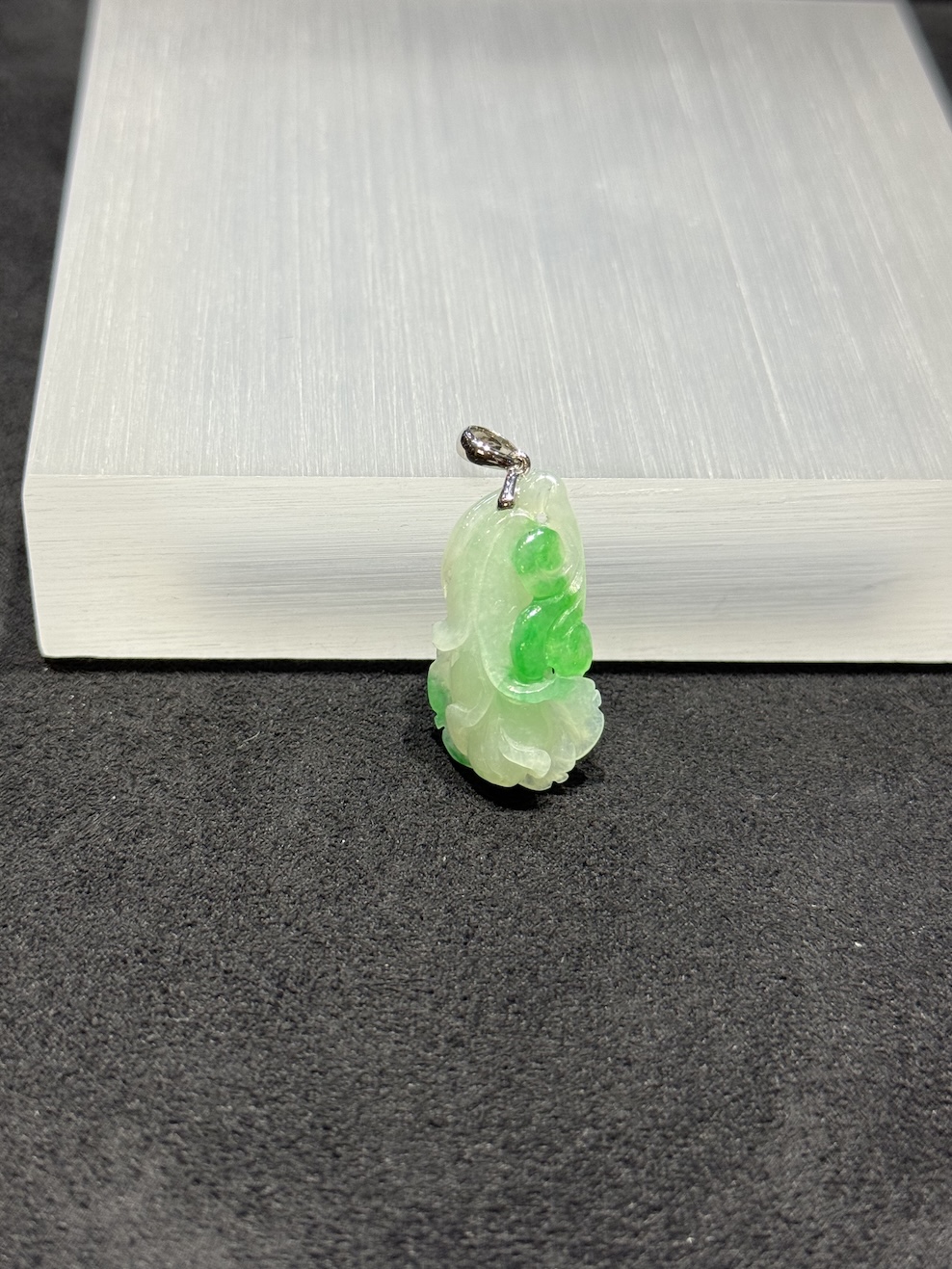 Ruyi jade pendant carved from translucent icy white and vibrant green jadeite, with a curling ruyi head and small flower bud details, hung from a 18k white gold bail