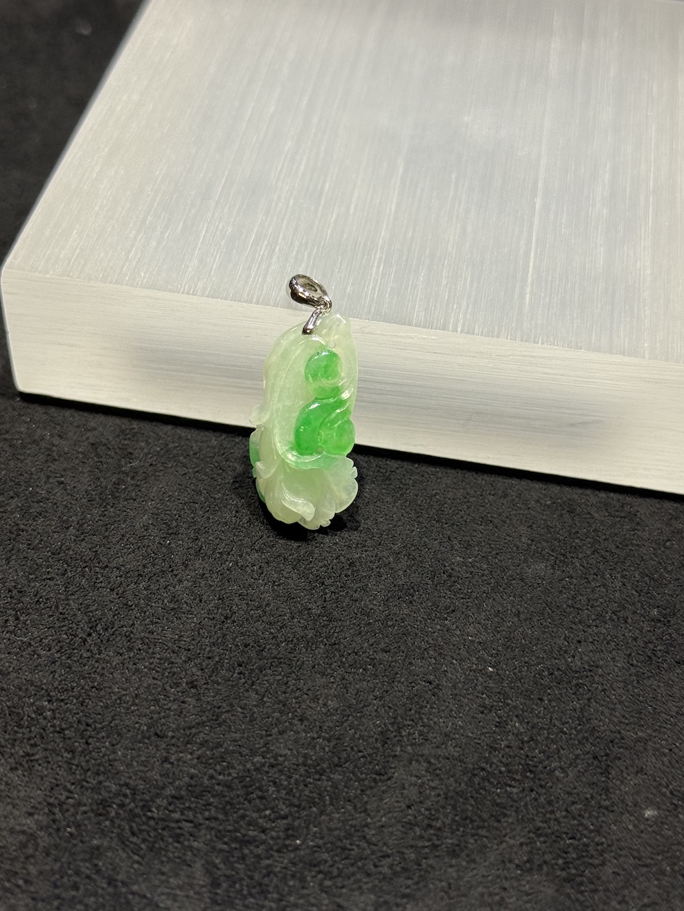 Ruyi jade pendant carved from translucent icy white and vibrant green jadeite, with a curling ruyi head and small flower bud details, hung from a 18k white gold bail