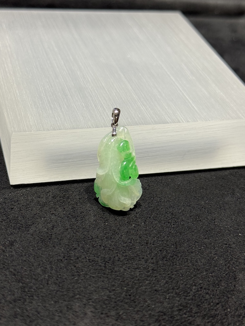 Ruyi jade pendant carved from translucent icy white and vibrant green jadeite, with a curling ruyi head and small flower bud details, hung from a 18k white gold bail