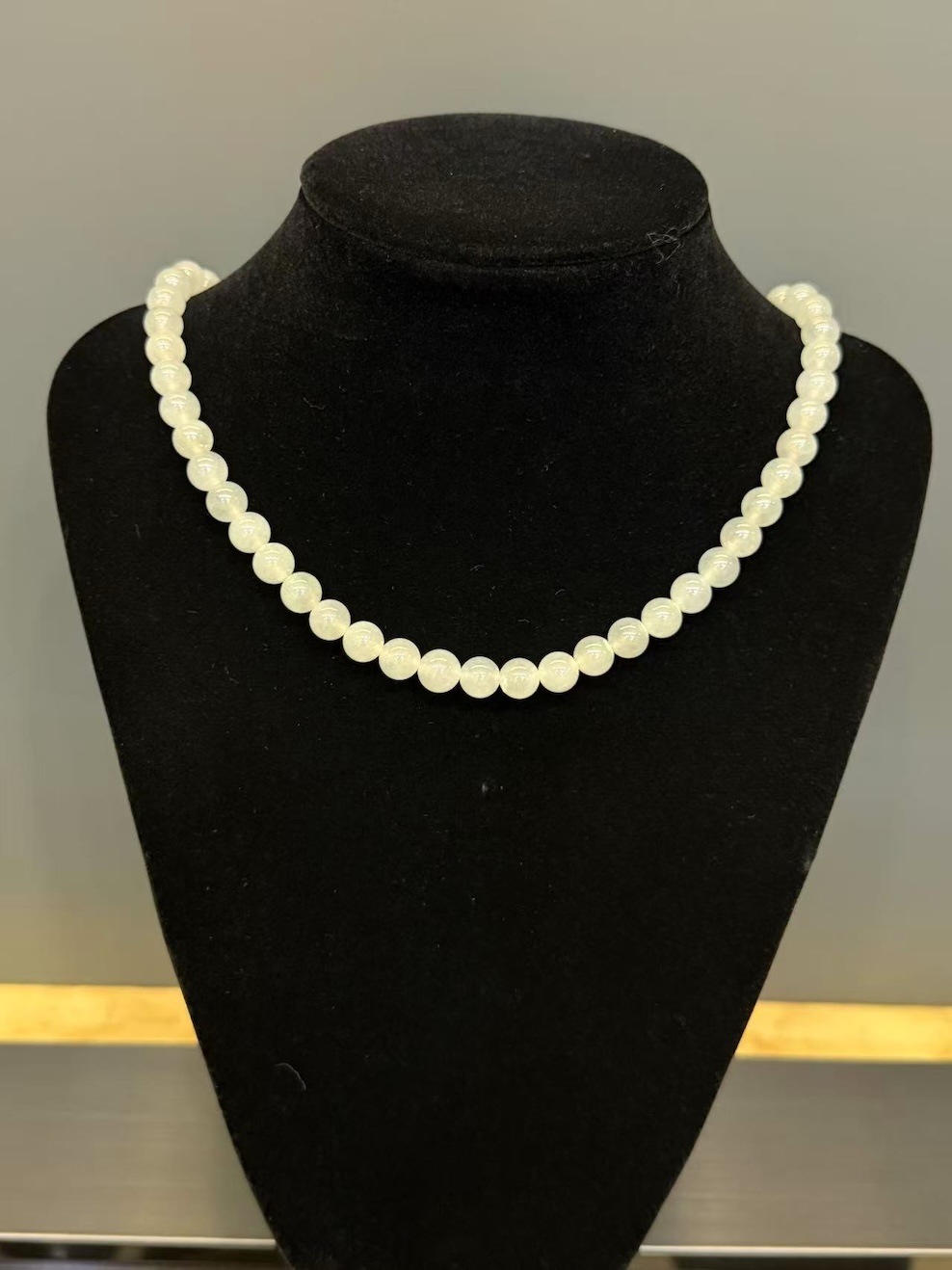Icy jadeite necklace strung with round translucent near-colourless jadeite beads in uniform size, shown looped on a black display cloth
