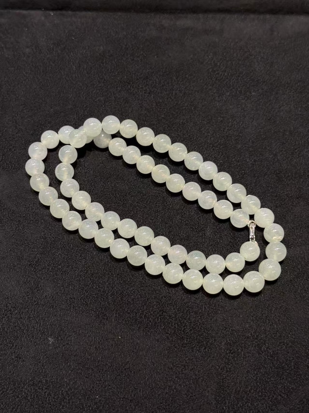 Icy jadeite necklace strung with round translucent near-colourless jadeite beads in uniform size, shown looped on a black display cloth