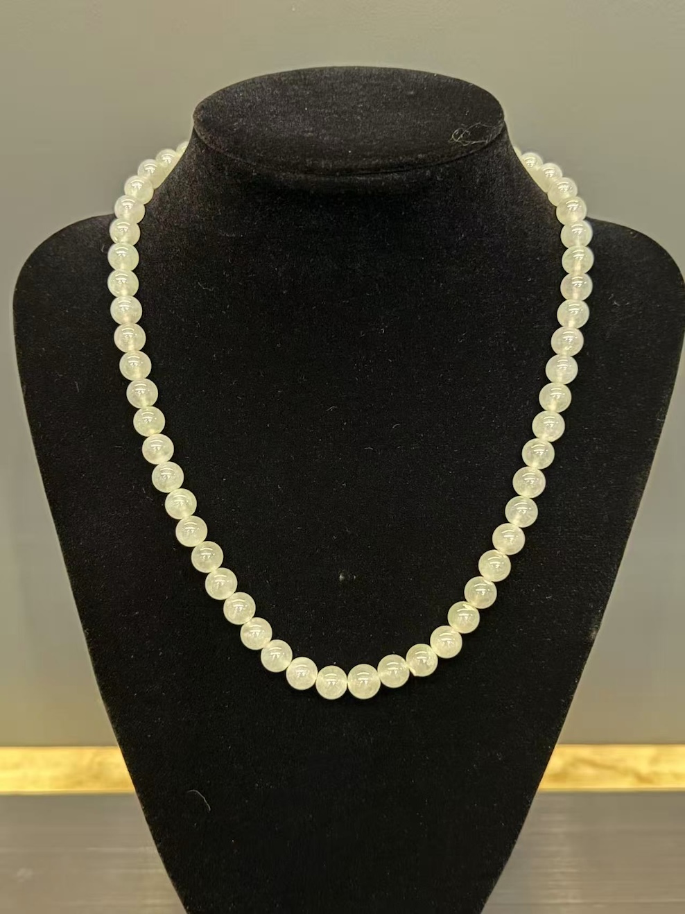 Icy jadeite necklace strung with round translucent near-colourless jadeite beads in uniform size, shown looped on a black display cloth