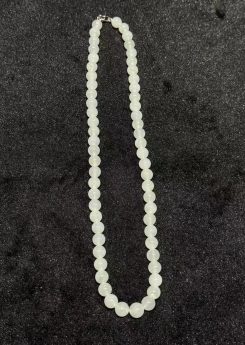 Icy jadeite necklace strung with round translucent near-colourless jadeite beads in uniform size, shown looped on a black display cloth