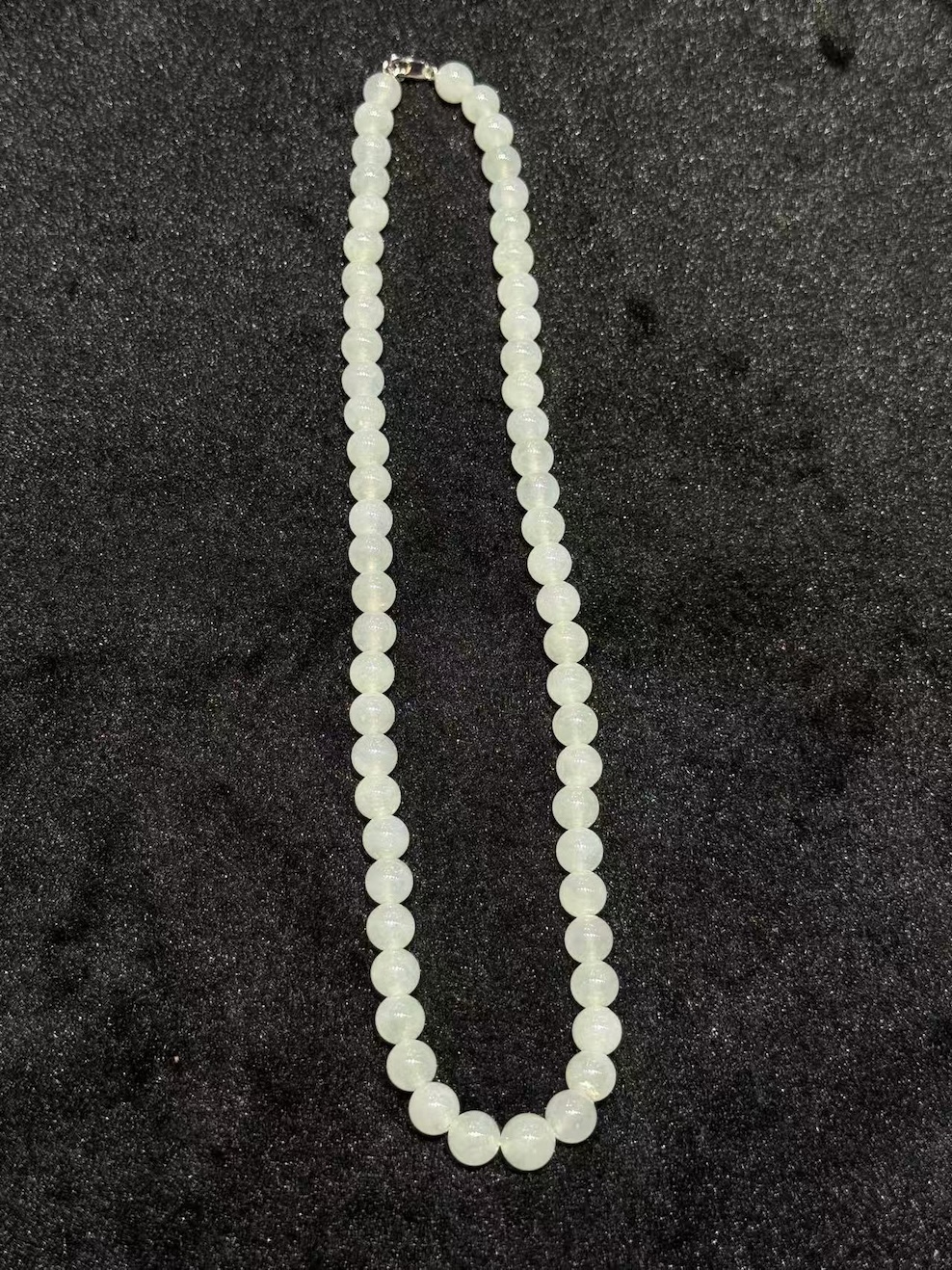 Icy jadeite necklace strung with round translucent near-colourless jadeite beads in uniform size, shown looped on a black display cloth