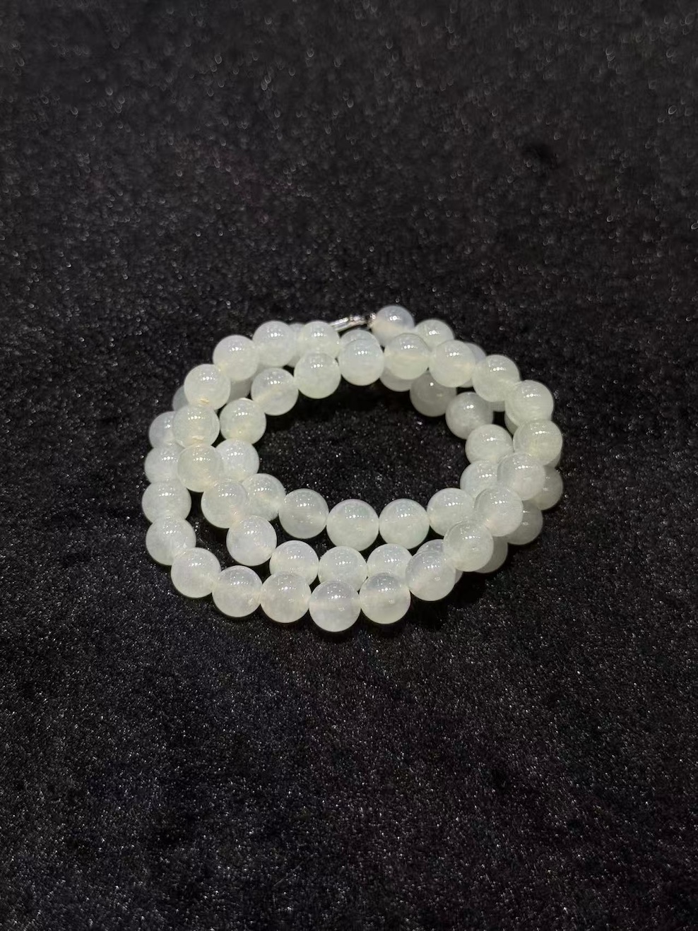 Icy jadeite necklace strung with round translucent near-colourless jadeite beads in uniform size, shown looped on a black display cloth