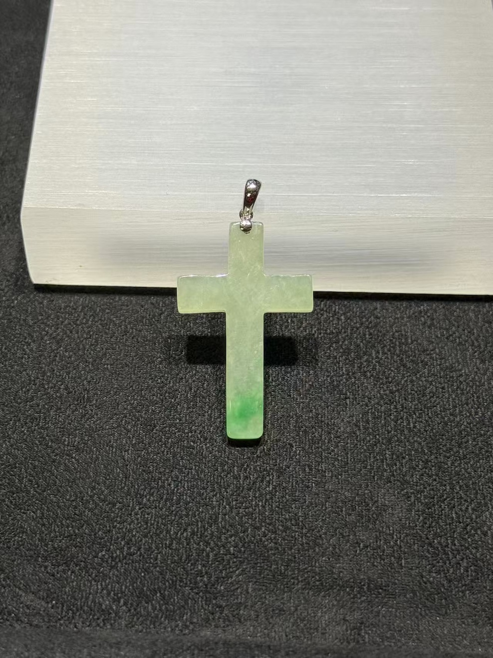 Jade cross pendant carved from translucent icy jadeite with vibrant green floating-flower patches, hung from a small 18k white gold bail