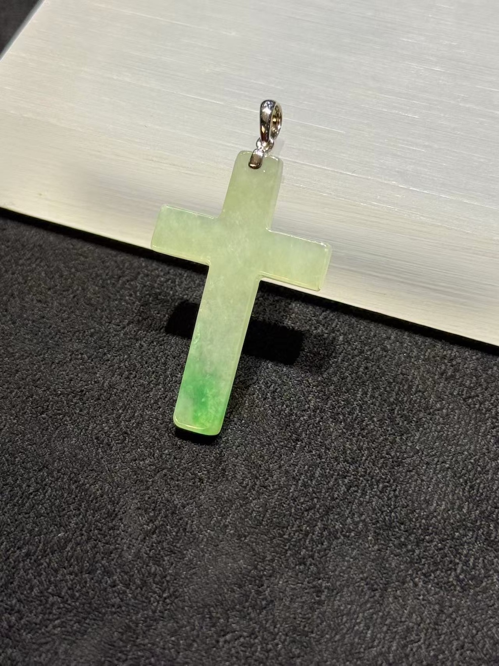 Jade cross pendant carved from translucent icy jadeite with vibrant green floating-flower patches, hung from a small 18k white gold bail