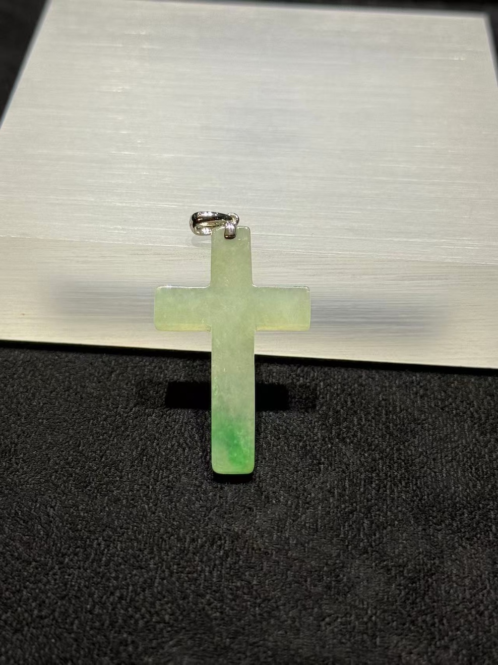 Jade cross pendant carved from translucent icy jadeite with vibrant green floating-flower patches, hung from a small 18k white gold bail