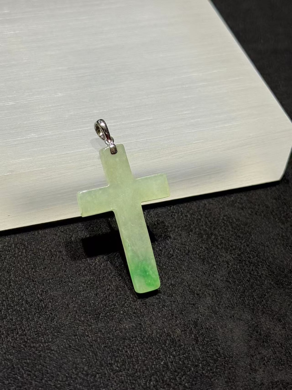 Jade cross pendant carved from translucent icy jadeite with vibrant green floating-flower patches, hung from a small 18k white gold bail
