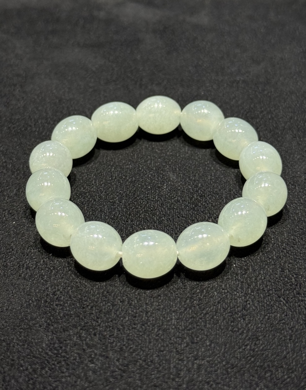 Icy jadeite bracelet strung with round translucent jadeite beads in a very faint, near-colourless green tone, shown on a dark display cloth