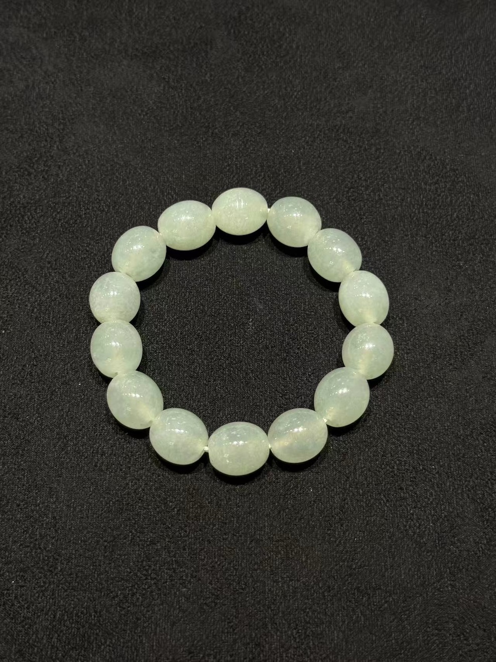 Icy jadeite bracelet strung with round translucent jadeite beads in a very faint, near-colourless green tone, shown on a dark display cloth