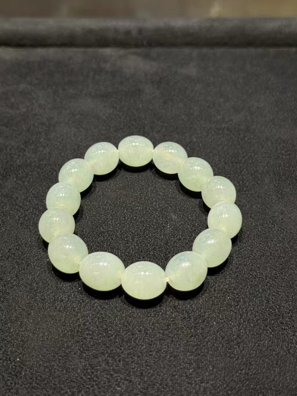 Icy jadeite bracelet strung with round translucent jadeite beads in a very faint, near-colourless green tone, shown on a dark display cloth