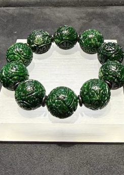 Carved jadeite bracelet strung with large dark green round beads, each cut with deep scrollwork and floral patterns, separated by small dark spacer beads
