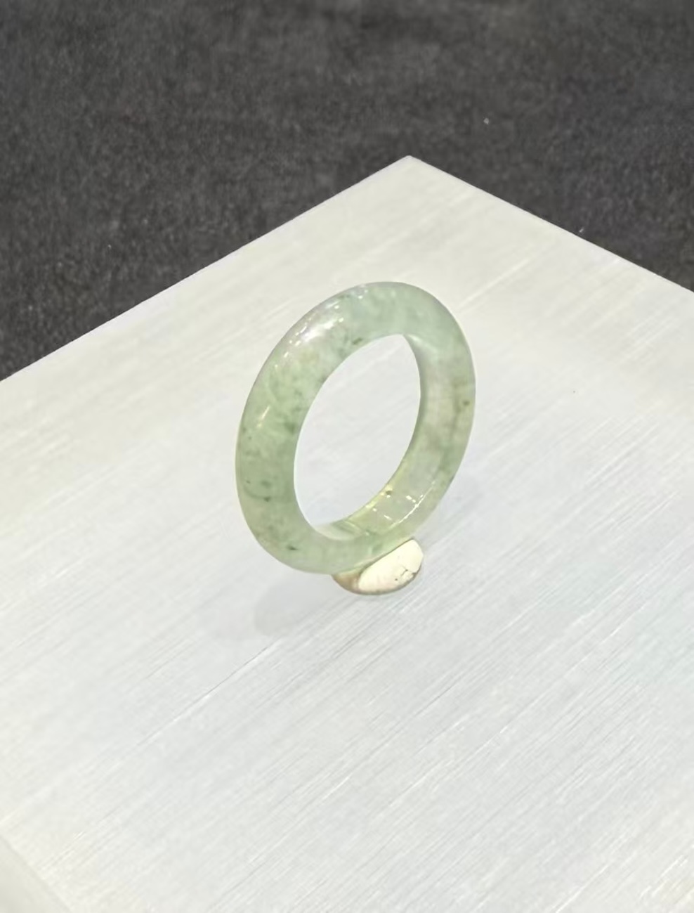 Icy jadeite ring carved as a wide solid band from a translucent, near-colourless jadeite with a faint green tint and small darker green flecks