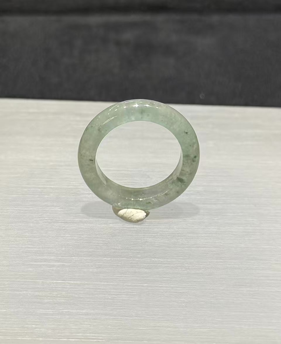 Icy jadeite ring carved as a wide solid band from a translucent, near-colourless jadeite with a faint green tint and small darker green flecks