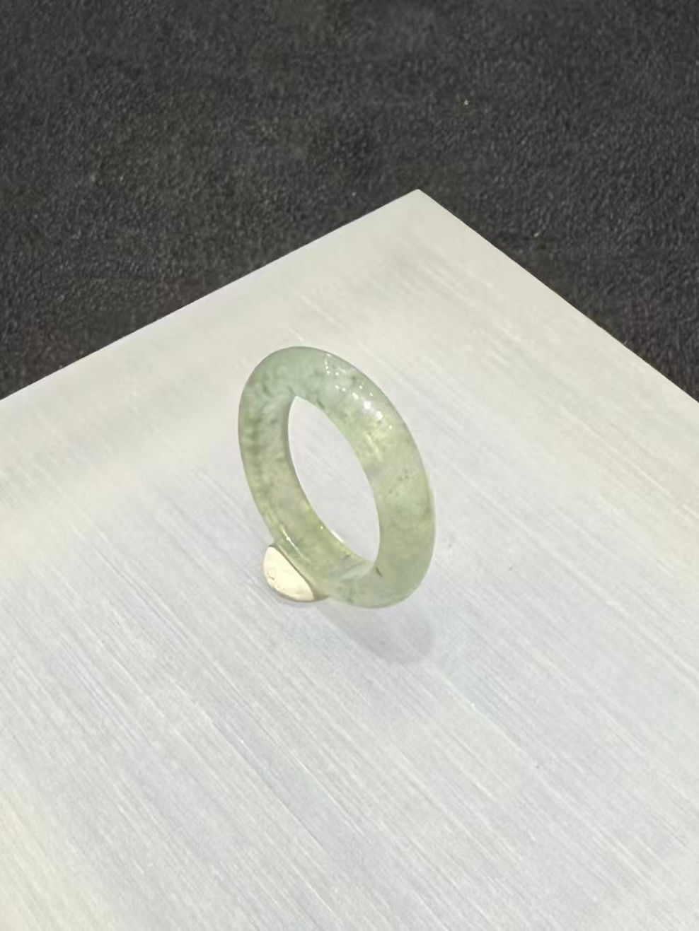 Icy jadeite ring carved as a wide solid band from a translucent, near-colourless jadeite with a faint green tint and small darker green flecks