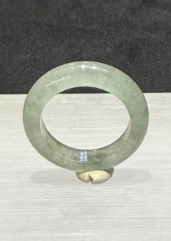 Icy jadeite ring carved as a wide solid band from a translucent, near-colourless jadeite with a faint green tint and small darker green flecks