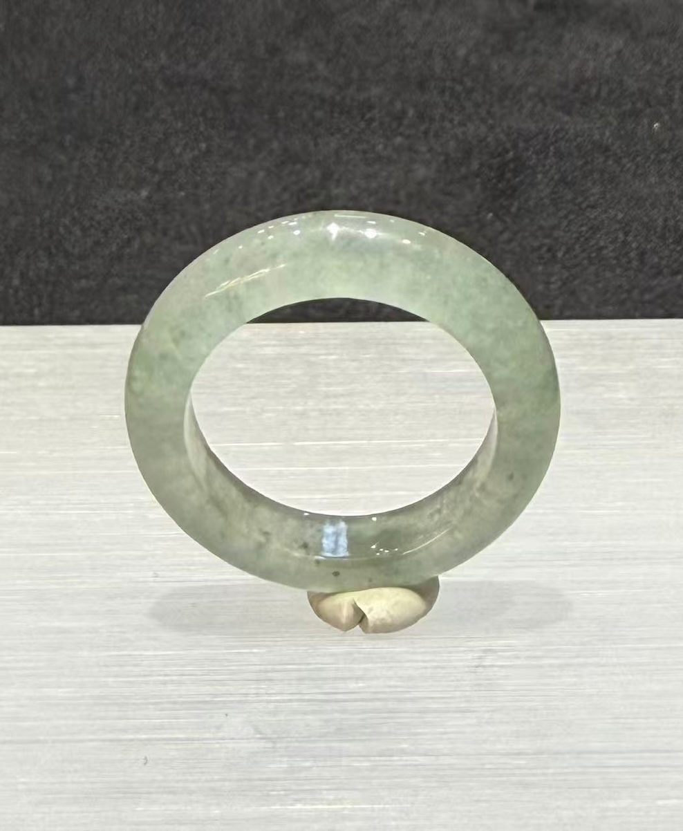 Icy jadeite ring carved as a wide solid band from a translucent, near-colourless jadeite with a faint green tint and small darker green flecks