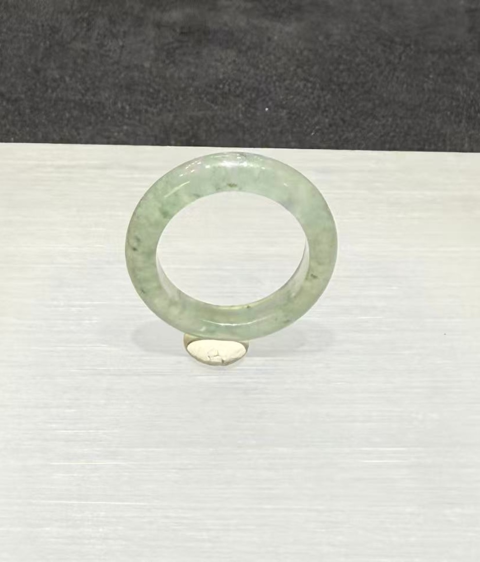 Icy jadeite ring carved as a wide solid band from a translucent, near-colourless jadeite with a faint green tint and small darker green flecks