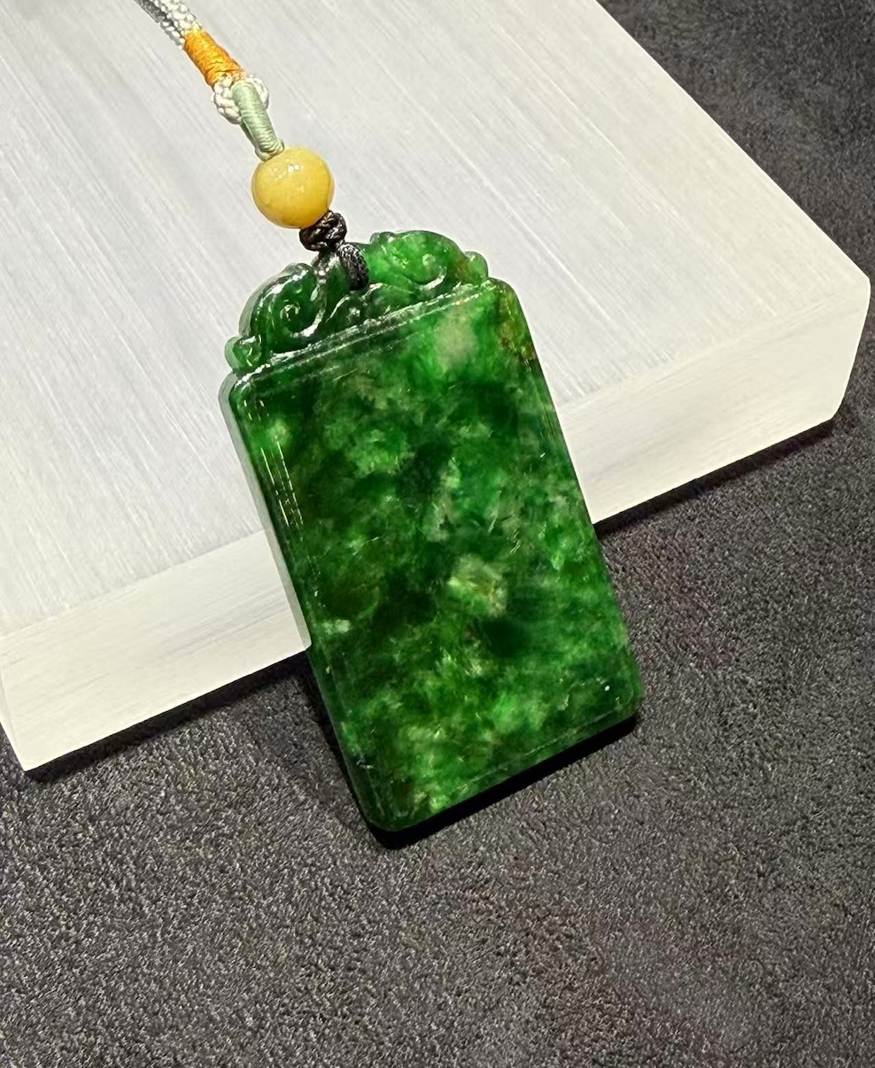 Old pit jadeite pendant carved as a rectangular pai-zi plaque from translucent vibrant deep green jadeite, with carved openwork scrollwork at the top and a smooth uncarved main face