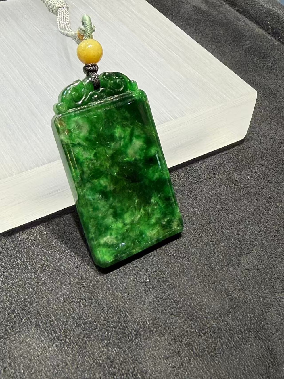 Old pit jadeite pendant carved as a rectangular pai-zi plaque from translucent vibrant deep green jadeite, with carved openwork scrollwork at the top and a smooth uncarved main face