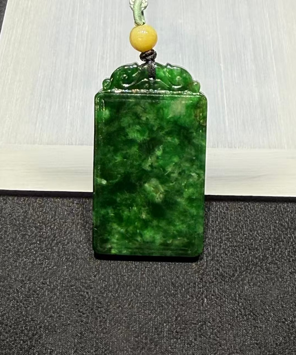 Old pit jadeite pendant carved as a rectangular pai-zi plaque from translucent vibrant deep green jadeite, with carved openwork scrollwork at the top and a smooth uncarved main face