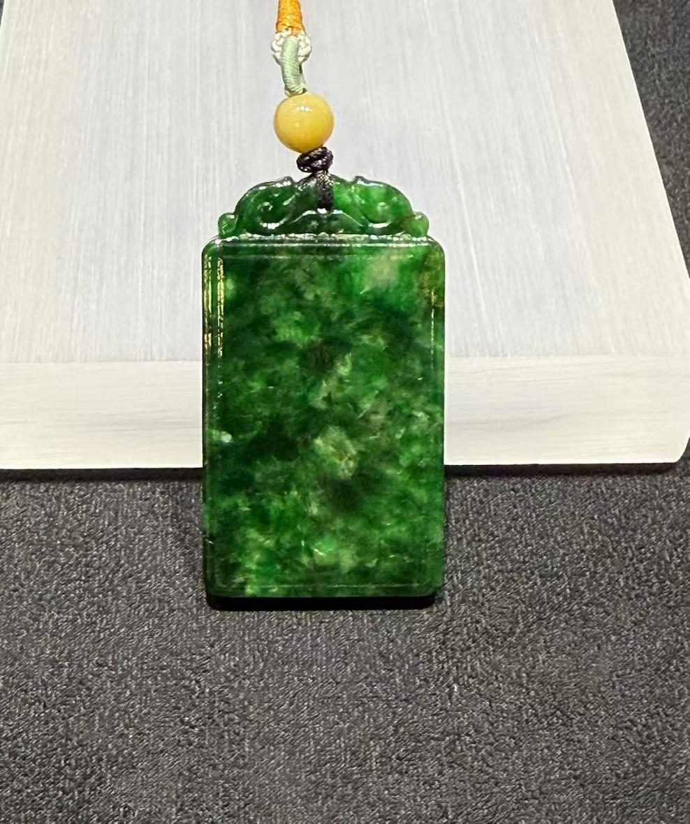 Old pit jadeite pendant carved as a rectangular pai-zi plaque from translucent vibrant deep green jadeite, with carved openwork scrollwork at the top and a smooth uncarved main face