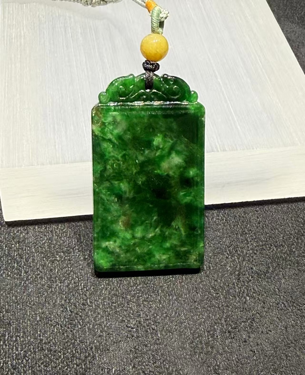 Old pit jadeite pendant carved as a rectangular pai-zi plaque from translucent vibrant deep green jadeite, with carved openwork scrollwork at the top and a smooth uncarved main face