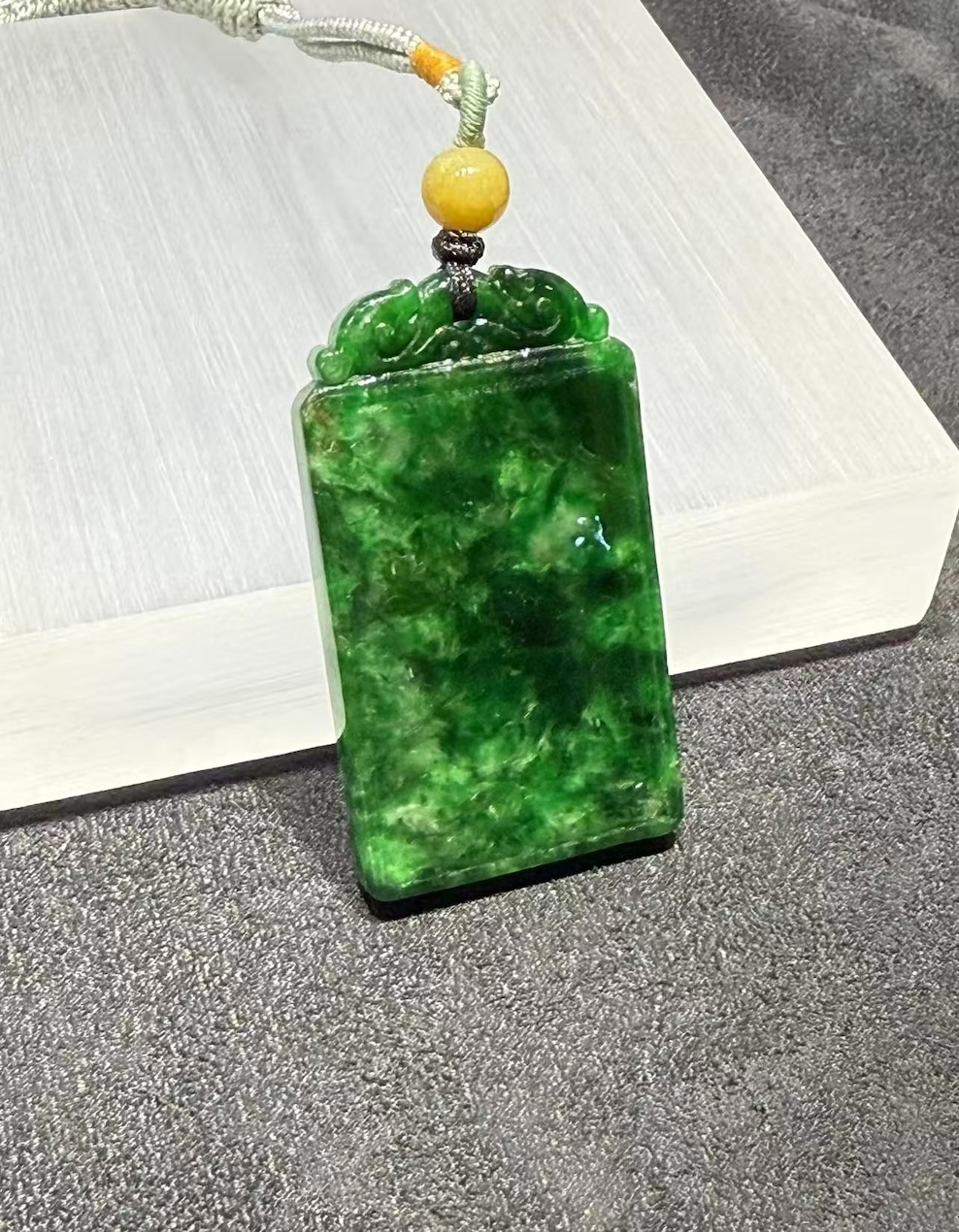 Old pit jadeite pendant carved as a rectangular pai-zi plaque from translucent vibrant deep green jadeite, with carved openwork scrollwork at the top and a smooth uncarved main face