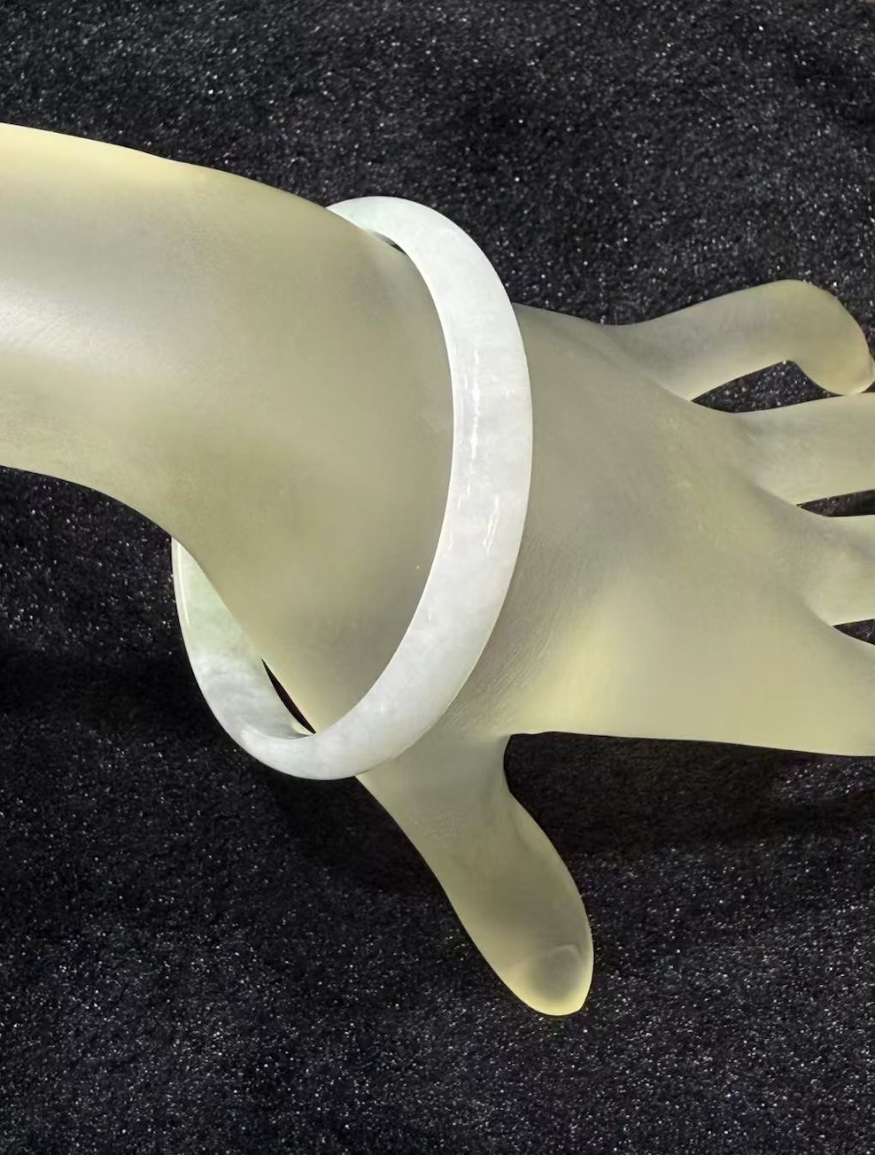 White jadeite bangle in a translucent whiteish body with very faint green tones drifting through the ring, shown on a frosted glass display hand
