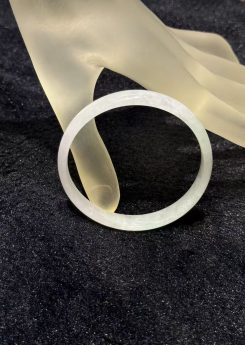 White jadeite bangle in a translucent whiteish body with very faint green tones drifting through the ring, shown on a frosted glass display hand