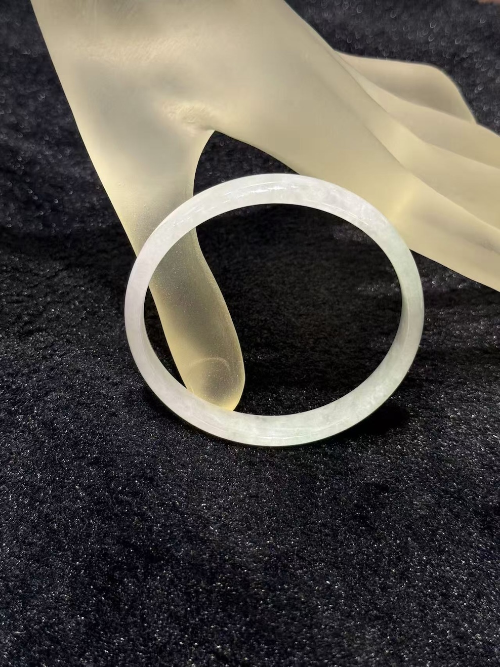 White jadeite bangle in a translucent whiteish body with very faint green tones drifting through the ring, shown on a frosted glass display hand