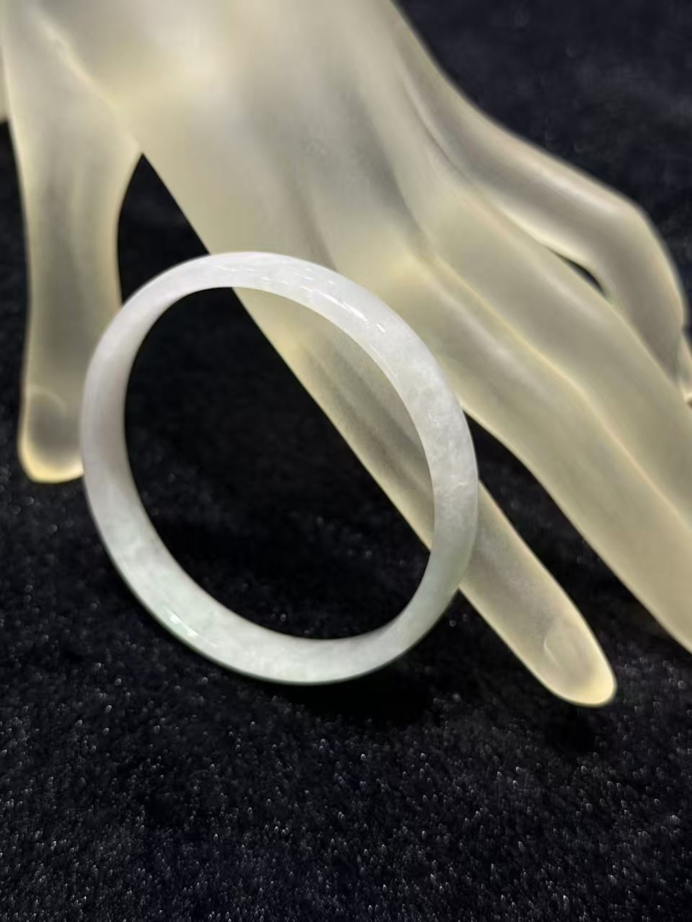 White jadeite bangle in a translucent whiteish body with very faint green tones drifting through the ring, shown on a frosted glass display hand
