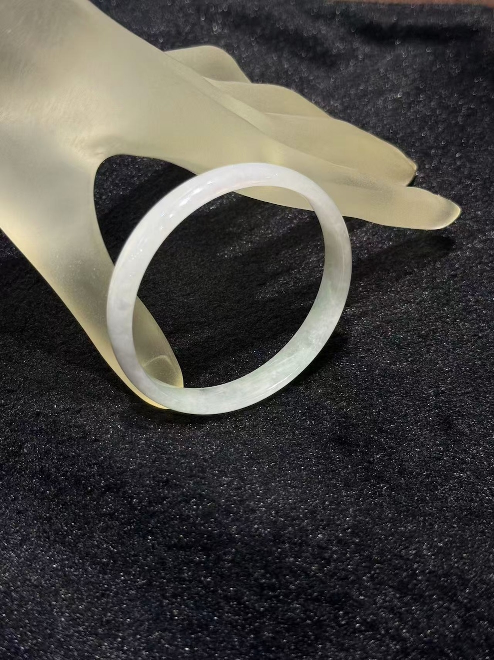 White jadeite bangle in a translucent whiteish body with very faint green tones drifting through the ring, shown on a frosted glass display hand