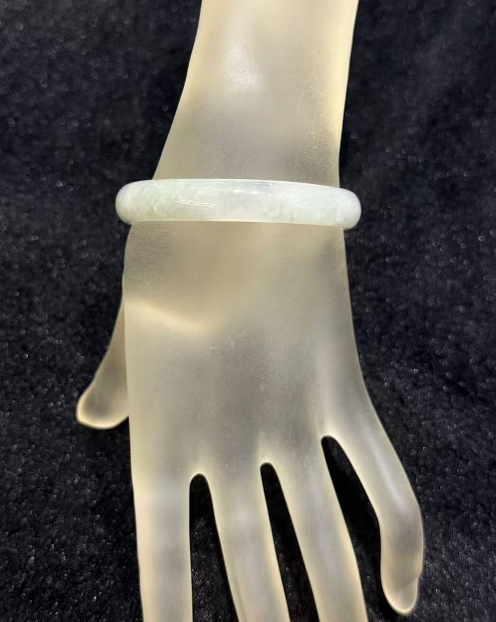 White jadeite bangle in a translucent whiteish body with very faint green tones drifting through the ring, shown on a frosted glass display hand
