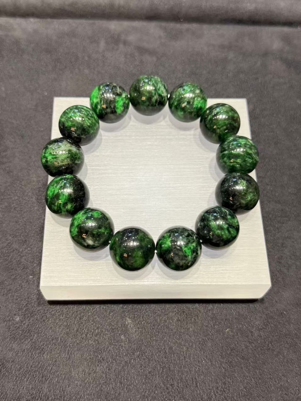 Vibrant green jadeite bracelet strung with large round beads showing deep dark green patches drifting through the vibrant green base