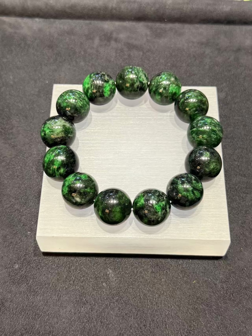 Vibrant green jadeite bracelet strung with large round beads showing deep dark green patches drifting through the vibrant green base