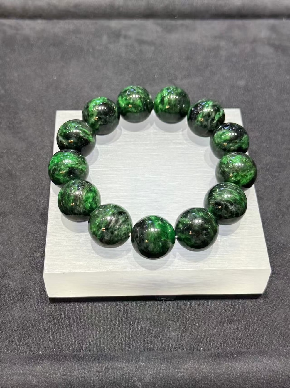 Vibrant green jadeite bracelet strung with large round beads showing deep dark green patches drifting through the vibrant green base