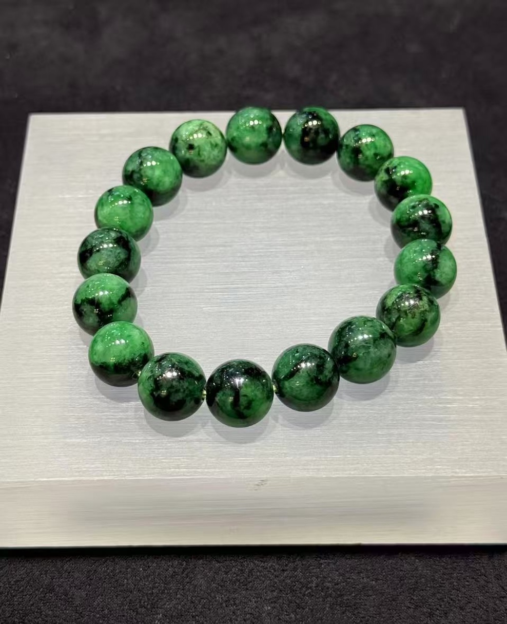 Old pit jadeite bracelet strung with large round beads in a translucent, vibrant deep green with darker patches and natural markings