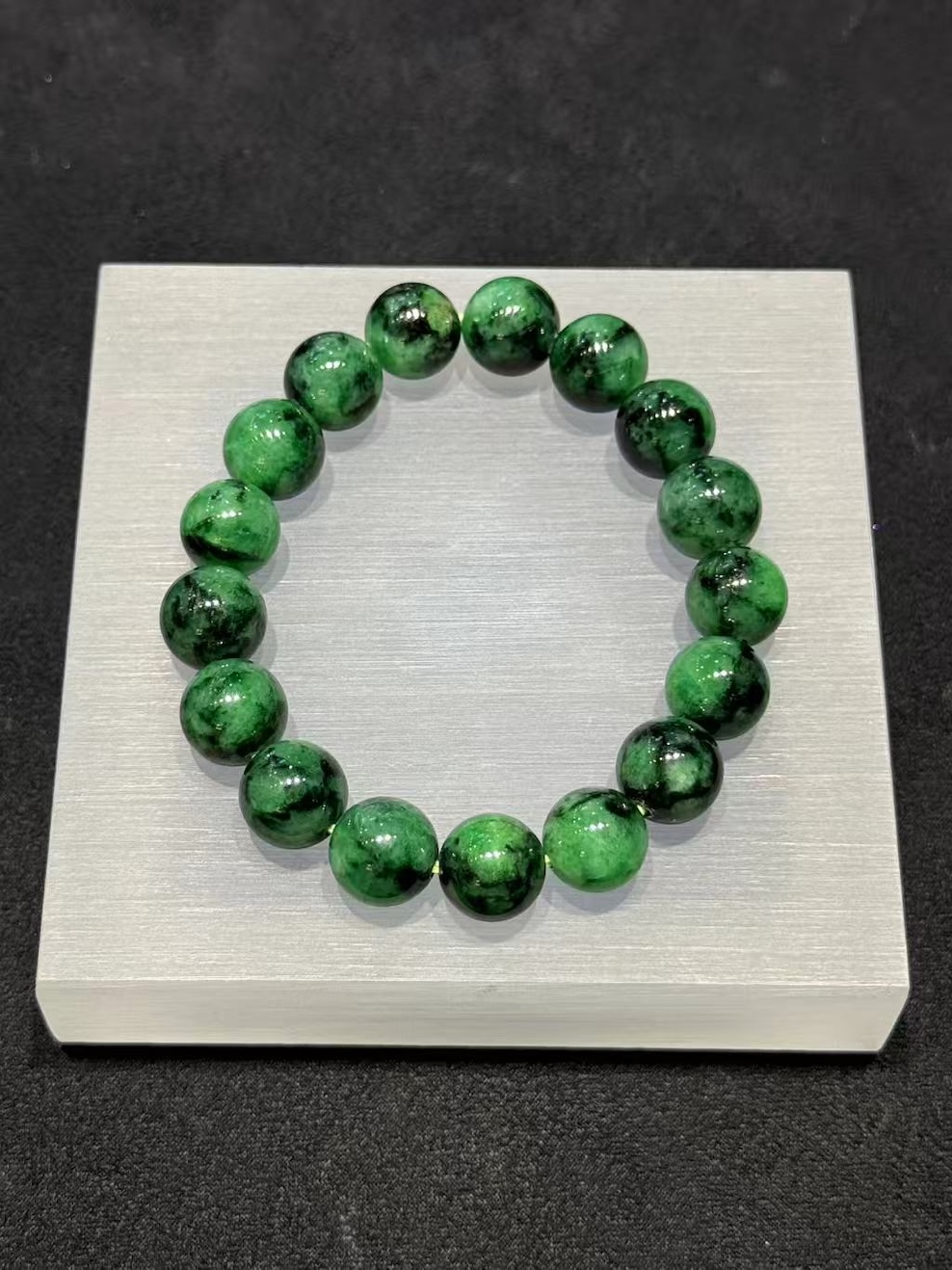 Old pit jadeite bracelet strung with large round beads in a translucent, vibrant deep green with darker patches and natural markings